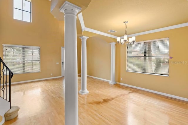 unfurnished dining area featuring crown molding, wood-type flooring, decorative columns, and a chandelier