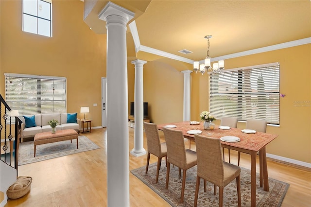 dining space featuring ornate columns, a high ceiling, ornamental molding, a notable chandelier, and light hardwood / wood-style flooring