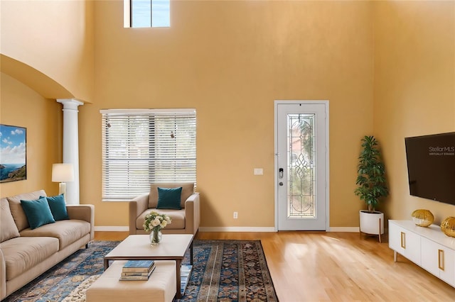 living room featuring a towering ceiling, light hardwood / wood-style floors, and ornate columns