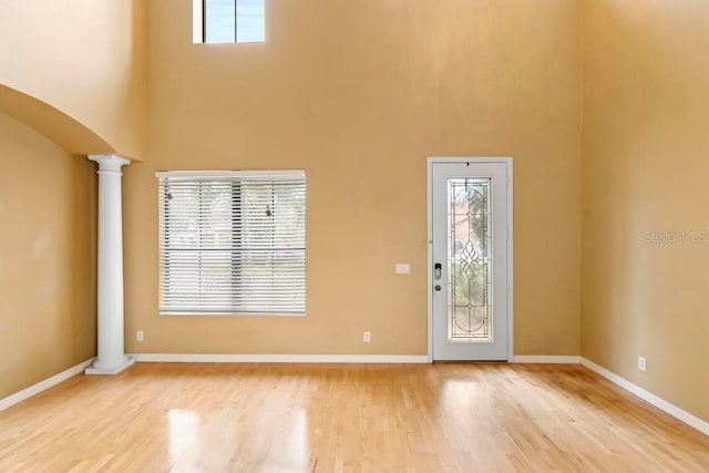 foyer entrance featuring a towering ceiling, decorative columns, and light wood-type flooring