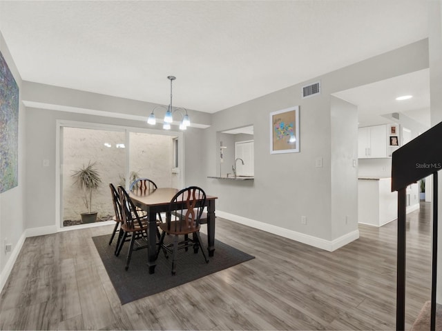 dining area featuring wood-type flooring, sink, and a chandelier