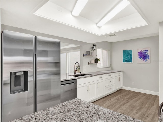 kitchen featuring sink, white cabinetry, light wood-type flooring, stainless steel appliances, and light stone countertops