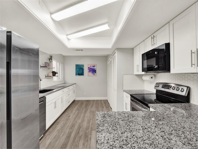 kitchen with stainless steel appliances, white cabinetry, sink, and light stone counters