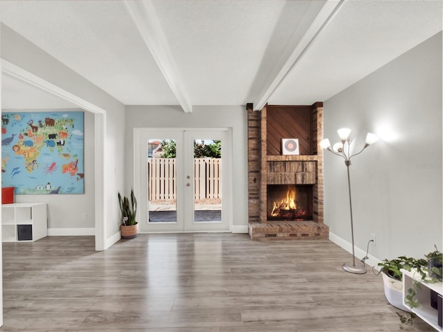 unfurnished living room with beamed ceiling, a fireplace, french doors, and hardwood / wood-style flooring