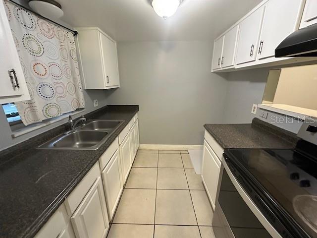 kitchen featuring light tile patterned floors, white cabinets, wall chimney exhaust hood, stainless steel range with electric cooktop, and a sink