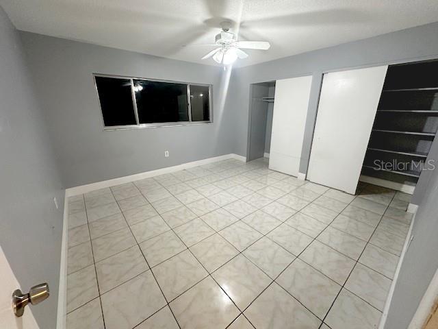 unfurnished bedroom featuring a ceiling fan, light tile patterned flooring, baseboards, and multiple closets