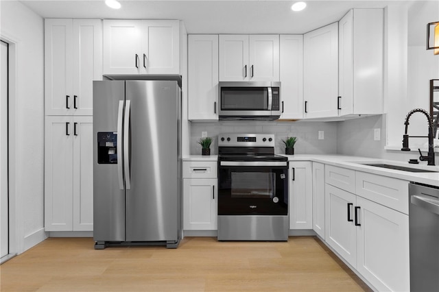 kitchen with sink, light wood-type flooring, white cabinets, and appliances with stainless steel finishes