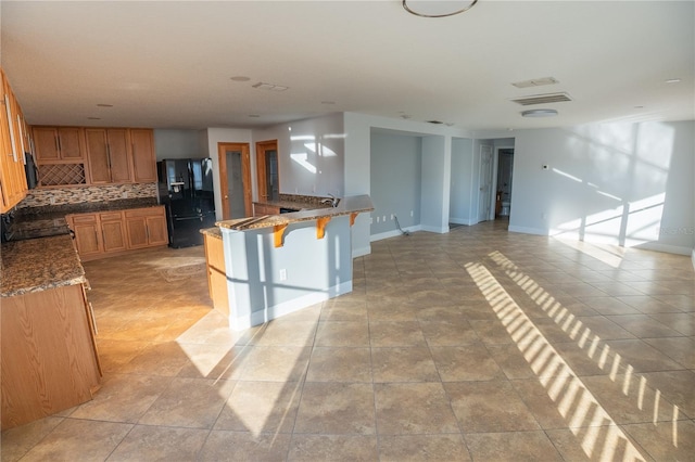 kitchen featuring sink, light tile patterned floors, a kitchen breakfast bar, tasteful backsplash, and black fridge with ice dispenser