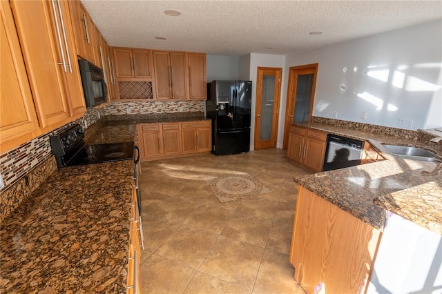 kitchen featuring sink, tasteful backsplash, a textured ceiling, dark stone counters, and black appliances