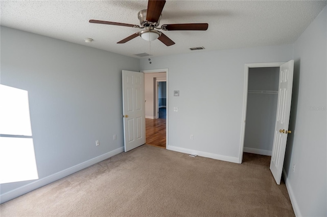 unfurnished bedroom with a spacious closet, light colored carpet, a textured ceiling, a closet, and ceiling fan