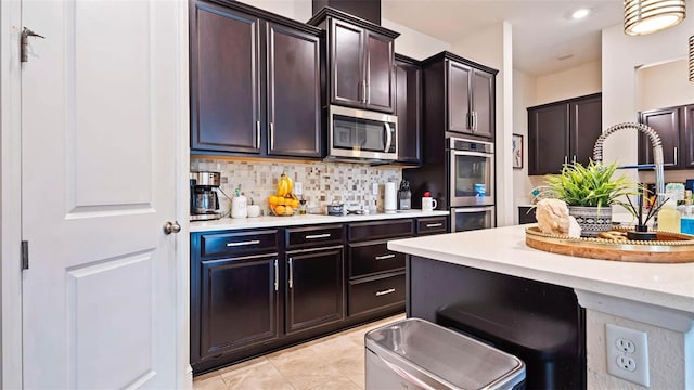 kitchen featuring dark brown cabinetry, light tile patterned floors, stainless steel appliances, light stone countertops, and decorative backsplash