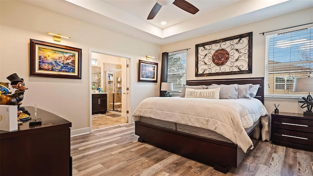 bedroom with a raised ceiling, wood-type flooring, connected bathroom, and ceiling fan