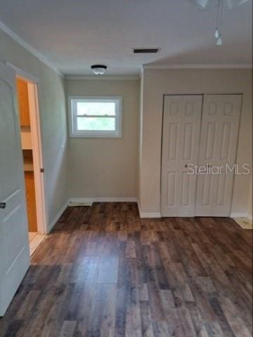 unfurnished bedroom featuring crown molding, dark wood-type flooring, and a closet