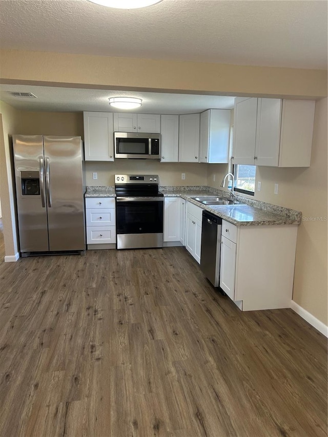 kitchen with dark wood-type flooring, sink, light stone counters, stainless steel appliances, and white cabinets