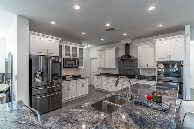 kitchen with appliances with stainless steel finishes, sink, white cabinets, backsplash, and wall chimney range hood