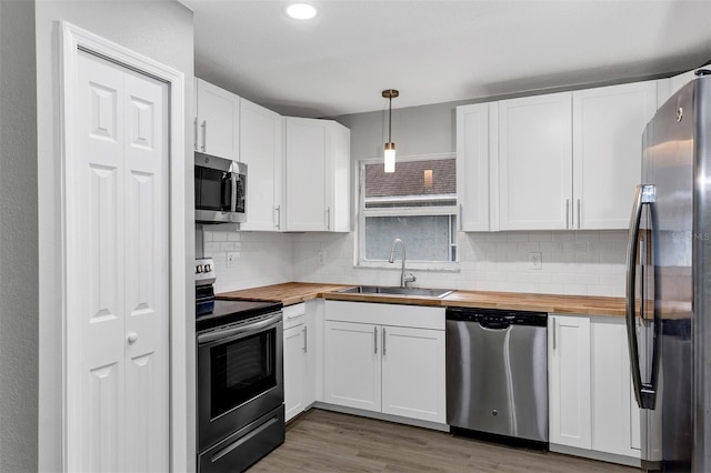 kitchen featuring sink, appliances with stainless steel finishes, butcher block counters, white cabinetry, and decorative light fixtures