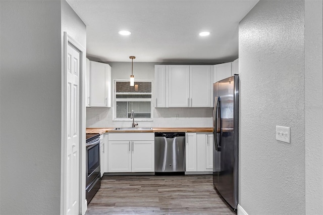 kitchen with butcher block countertops, decorative light fixtures, sink, white cabinets, and stainless steel appliances