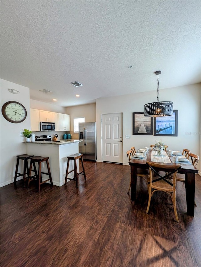 dining room with baseboards, a textured ceiling, visible vents, and dark wood-type flooring