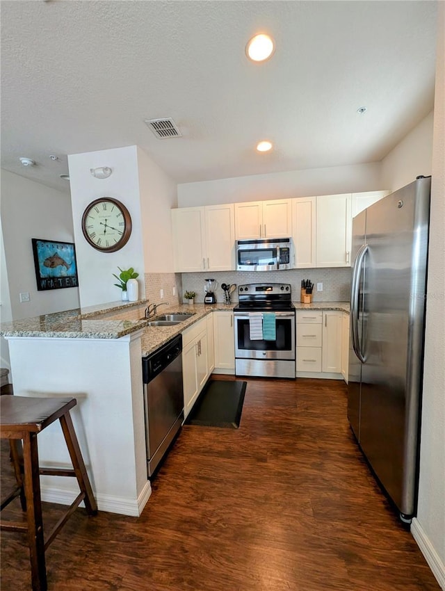 kitchen with dark wood finished floors, stainless steel appliances, light stone countertops, a peninsula, and a kitchen breakfast bar