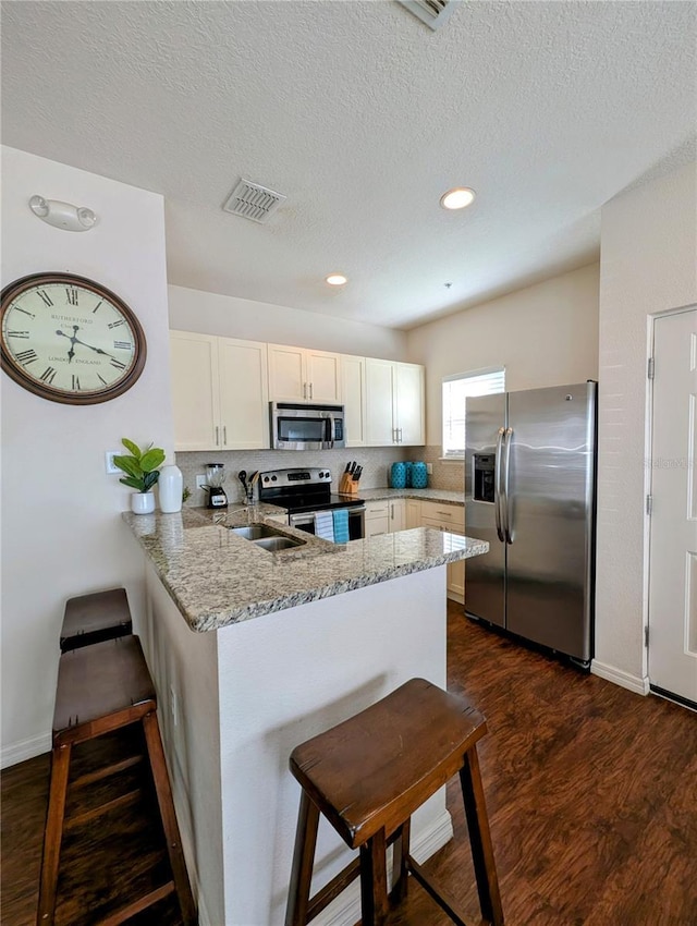 kitchen featuring a peninsula, visible vents, appliances with stainless steel finishes, light stone countertops, and dark wood finished floors