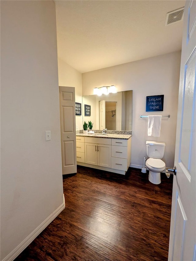 bathroom with visible vents, toilet, vanity, wood finished floors, and baseboards