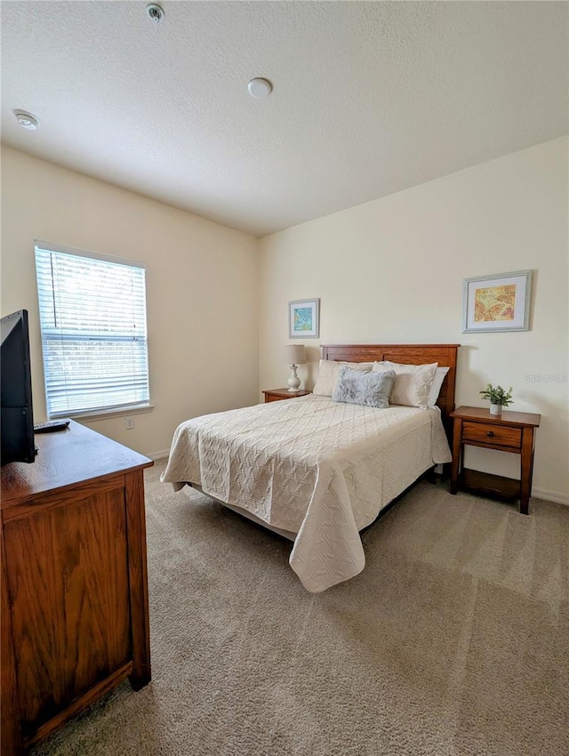 bedroom with baseboards, a textured ceiling, and light colored carpet