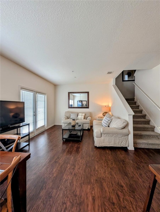 living room with a textured ceiling, stairs, baseboards, and dark wood-type flooring