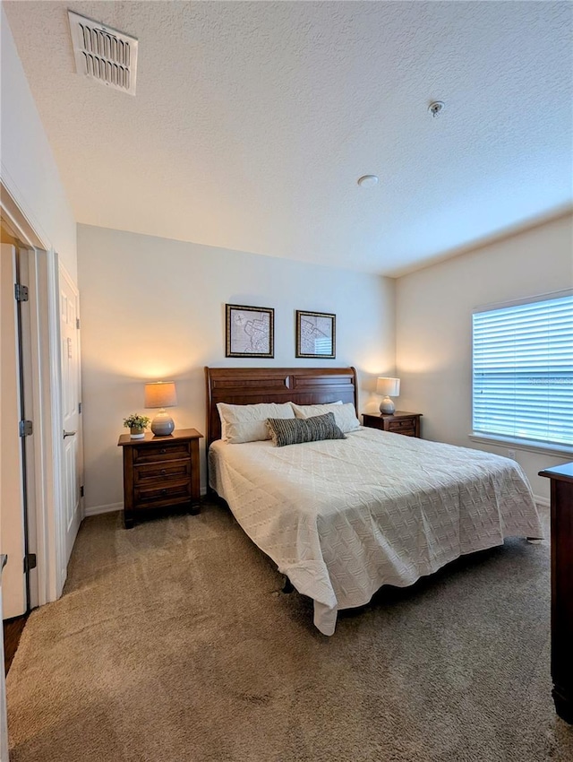 carpeted bedroom featuring a textured ceiling, visible vents, and baseboards