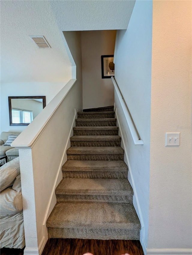 stairs with a textured ceiling, wood finished floors, visible vents, and baseboards