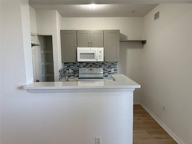 kitchen featuring gray cabinetry, tasteful backsplash, hardwood / wood-style flooring, kitchen peninsula, and range with electric cooktop