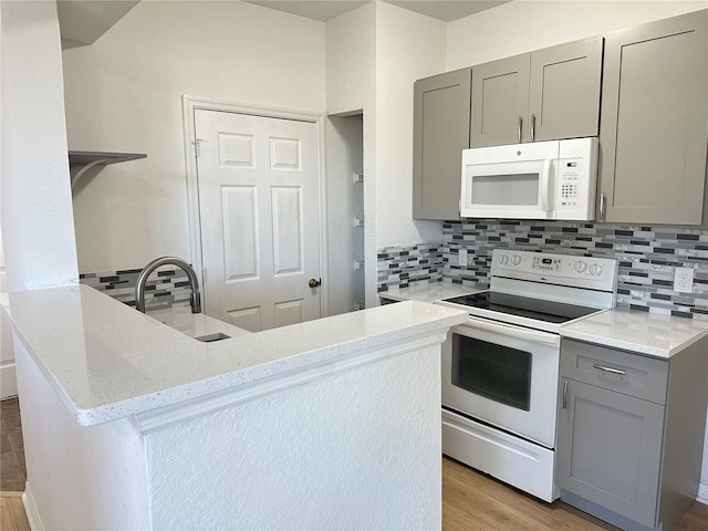 kitchen with light stone counters, white appliances, gray cabinets, and kitchen peninsula