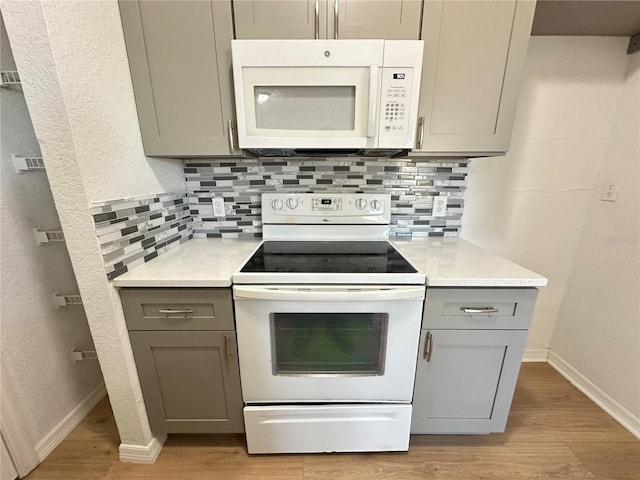 kitchen with tasteful backsplash, white appliances, gray cabinets, and light wood-type flooring