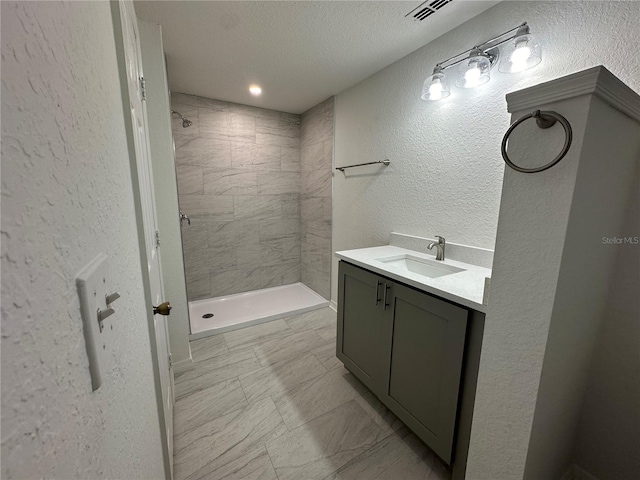 bathroom with vanity, a textured ceiling, and a tile shower