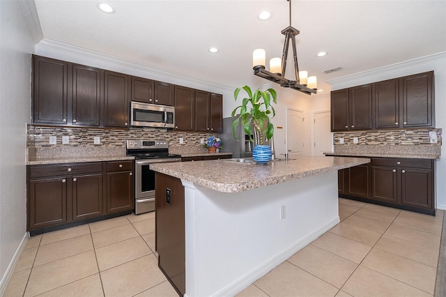 kitchen with ornamental molding, light tile patterned floors, stainless steel appliances, dark brown cabinets, and a center island with sink