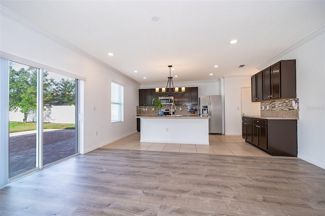 kitchen with tasteful backsplash, appliances with stainless steel finishes, decorative light fixtures, and an island with sink