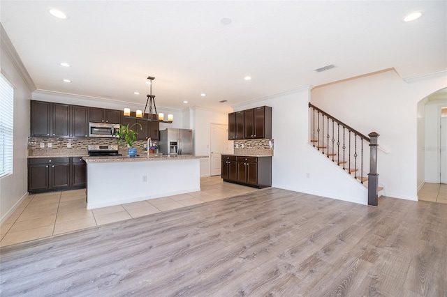 kitchen featuring dark brown cabinetry, tasteful backsplash, a center island with sink, stainless steel appliances, and light hardwood / wood-style floors