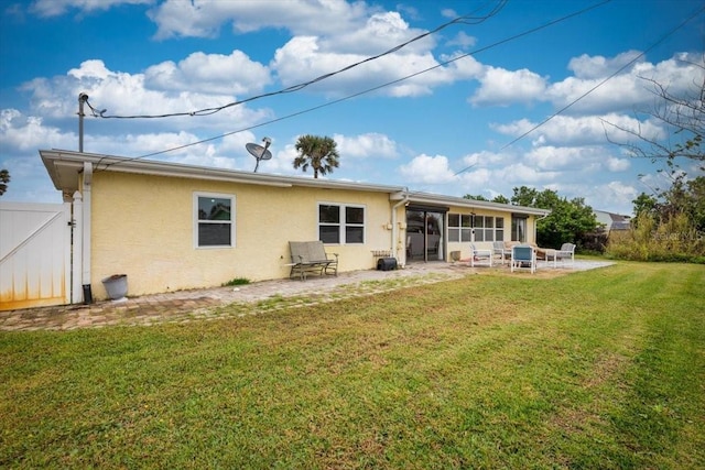 rear view of house with a yard, a patio, stucco siding, a sunroom, and a gate