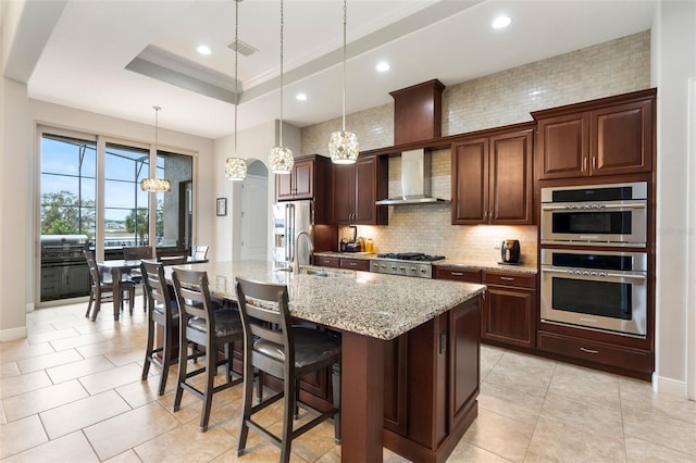 kitchen featuring sink, a breakfast bar area, light stone counters, an island with sink, and pendant lighting