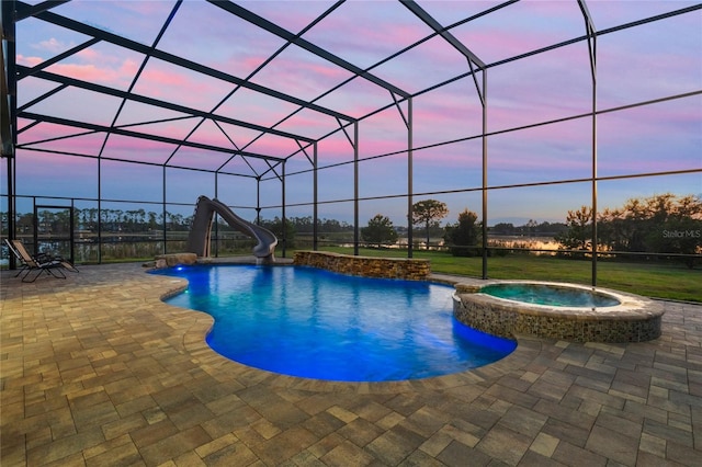 pool at dusk with a water slide, a patio area, an in ground hot tub, and glass enclosure