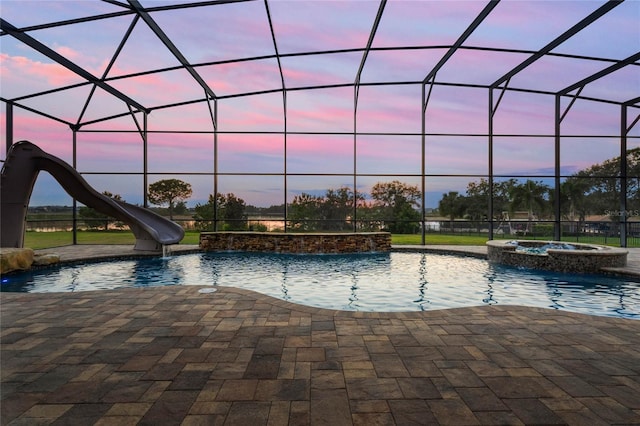 pool at dusk featuring an in ground hot tub, a water slide, a lanai, and a patio