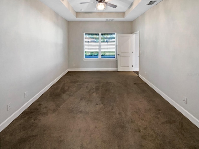 spare room featuring dark colored carpet, ceiling fan, and a tray ceiling