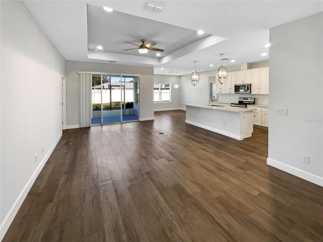 unfurnished living room with ceiling fan with notable chandelier, dark hardwood / wood-style flooring, a raised ceiling, and sink