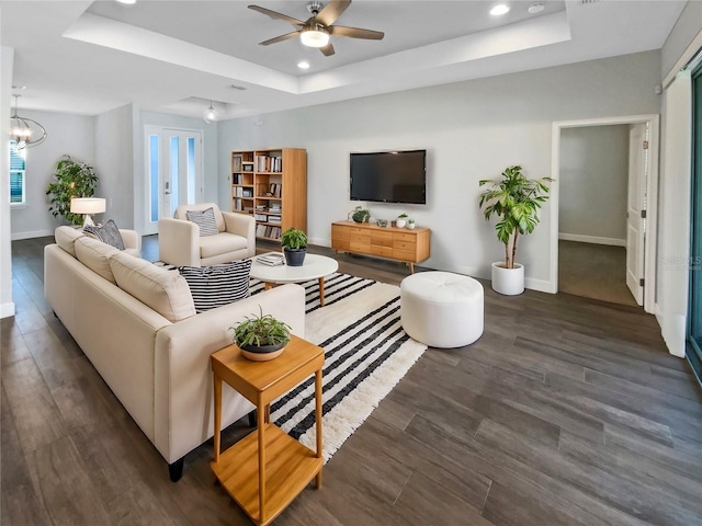 living room with dark wood-type flooring, a tray ceiling, and ceiling fan with notable chandelier