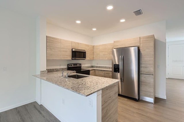kitchen featuring light stone counters, a peninsula, visible vents, appliances with stainless steel finishes, and a sink