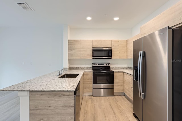 kitchen with light brown cabinets, a peninsula, visible vents, stainless steel appliances, and a sink