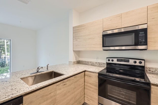 kitchen with light stone countertops, a peninsula, a sink, stainless steel appliances, and light brown cabinets