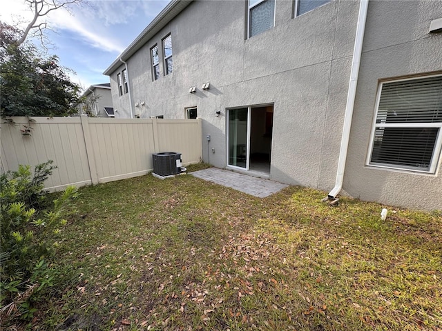 rear view of house featuring central AC, stucco siding, fence private yard, and a lawn
