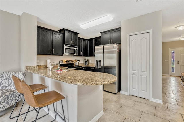kitchen with a breakfast bar, sink, light stone counters, appliances with stainless steel finishes, and kitchen peninsula