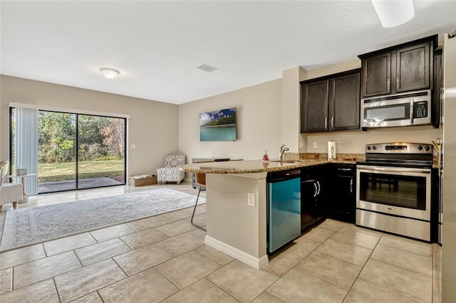 kitchen with light stone counters, dark brown cabinets, light tile patterned floors, kitchen peninsula, and stainless steel appliances
