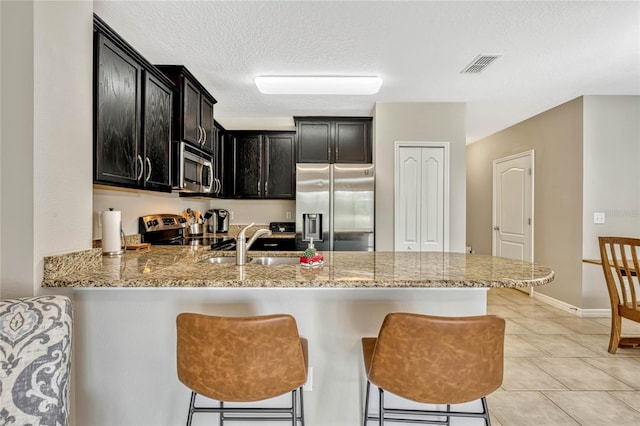 kitchen with sink, light stone counters, appliances with stainless steel finishes, a kitchen breakfast bar, and kitchen peninsula